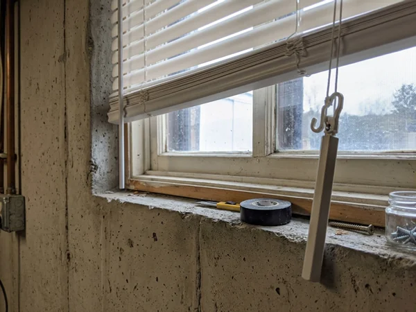 Cordless vinyl blind bottom rail and tilt wand on a furnace room window